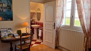 Une pièce comprenant une table en bois, une chaise, un bureau avec une lampe, un miroir, un lavabo et une fenêtre avec des rideaux.