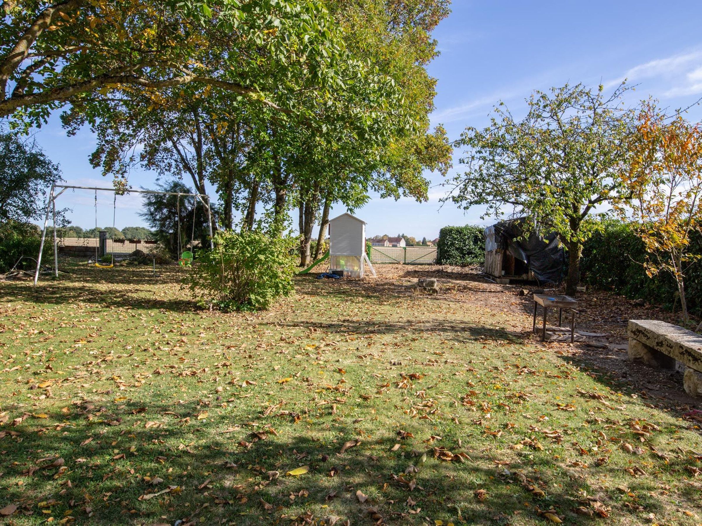 Un jardin avec une balançoire, un petit abri de jardin et un banc en pierre.