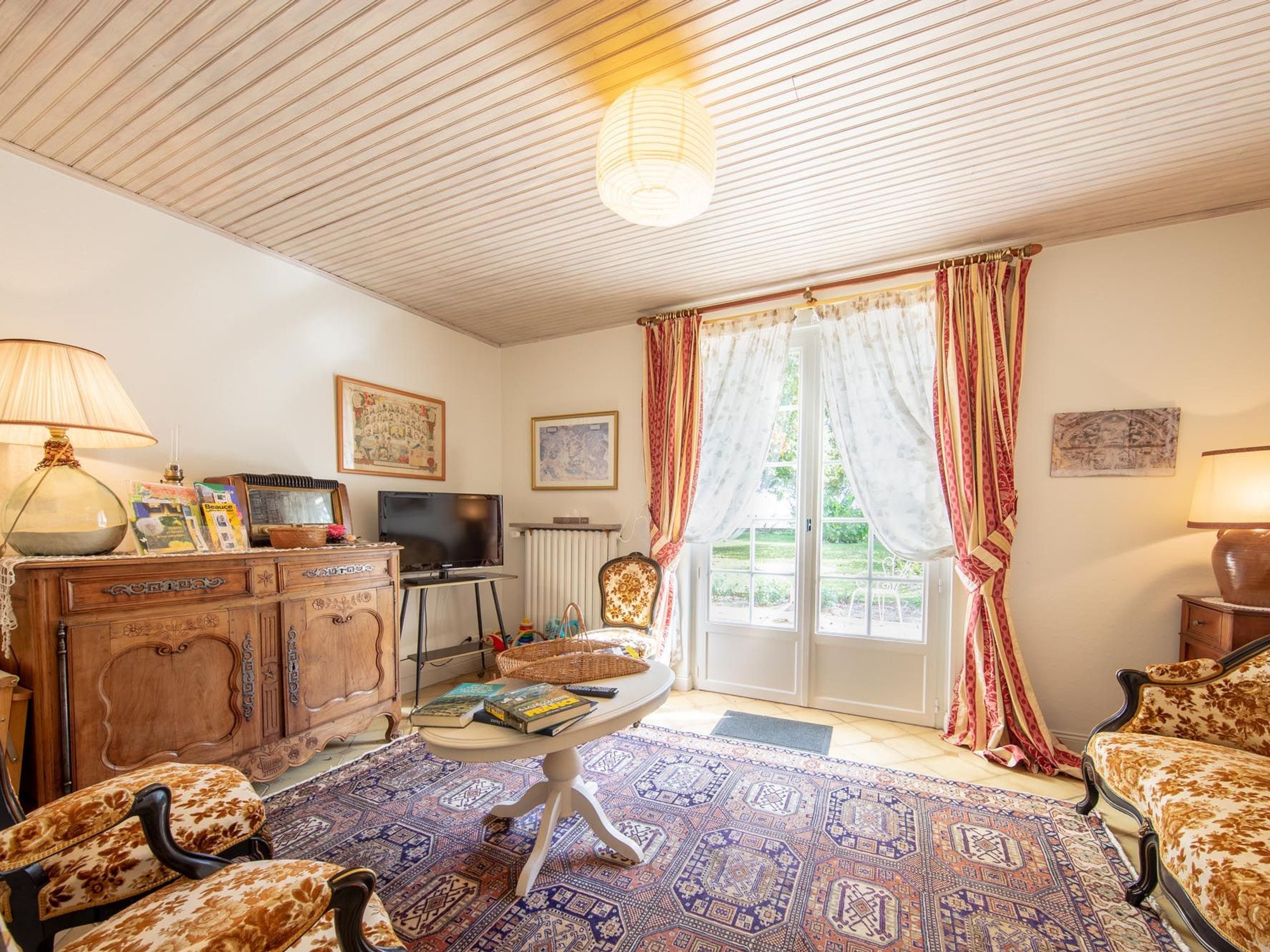 Un salon chaleureux avec un plafond en bois, une télévision, une cheminée et une grande fenêtre avec des rideaux.