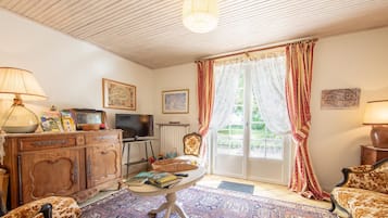 Un salon chaleureux avec un plafond en bois, une télévision, une cheminée et une grande fenêtre avec des rideaux.