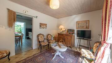 Sala de estar com tapete estampado, móveis de madeira, televisão e uma área de jantar visível através de uma porta aberta.