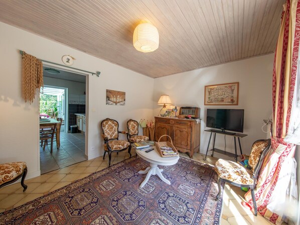 A living room with a patterned rug, wooden furniture, a television, and a dining area visible through an open door. - Room La Loire - Disabled Access, WiFi, Pets Allowed (Saint-Benoît-sur-Loire)