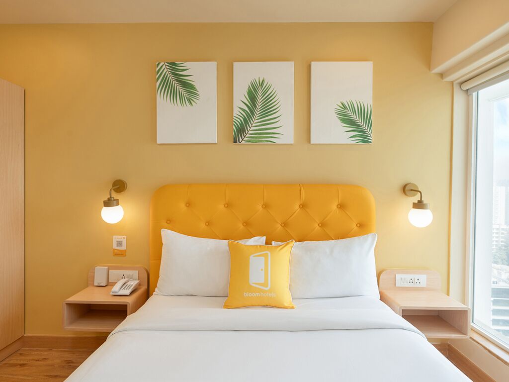 A hotel room with a yellow headboard, white bedding, and three palm leaf wall art pieces.