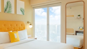 A hotel room with a large bed, a city view through the window, a mirror, and a bedside table with a lamp. - Bloom Hotel Saki Vihar (Mumbai)