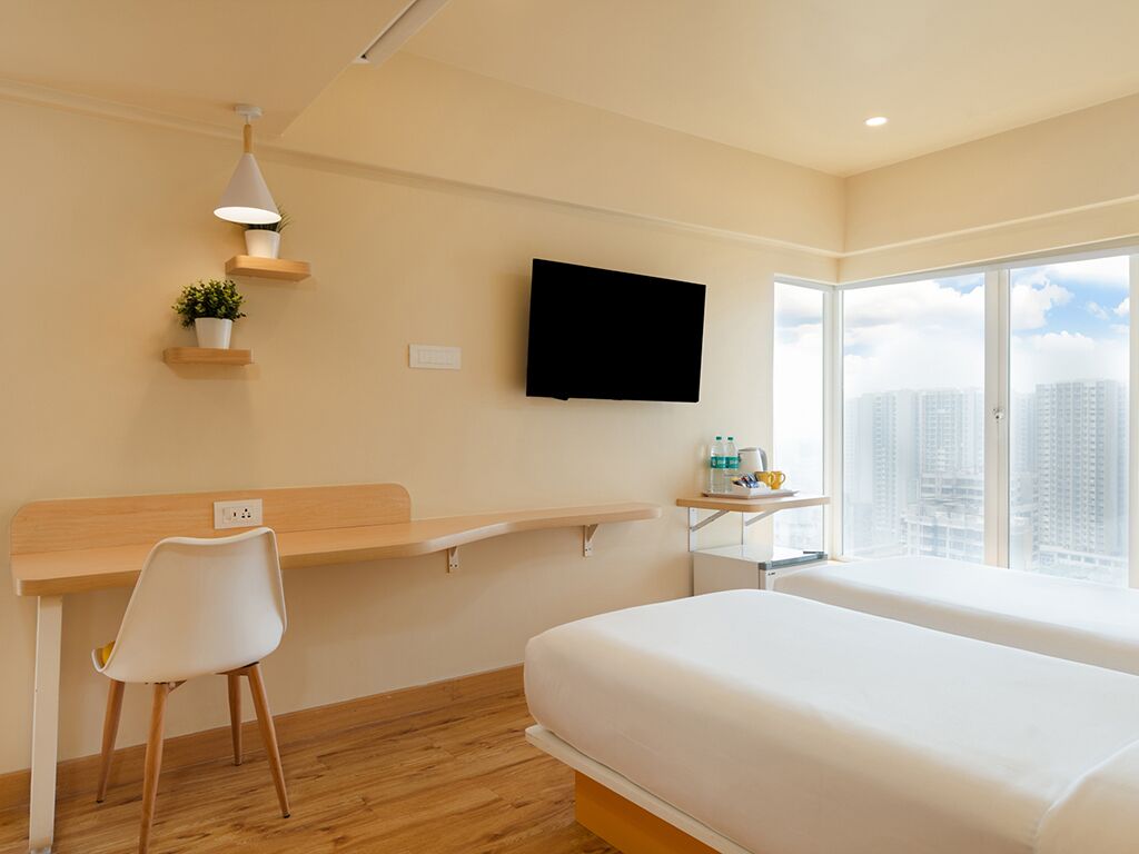 Une chambre d’hôtel équipée d’un lit, d’un bureau, d’une chaise, d’une télévision et d’une fenêtre donnant sur la ville.