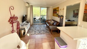 A compact living space with a sofa, a small table, and a TV. There is a sliding glass door leading to an outdoor area. - City Escape Getaway Subiaco 1Bedrm Unit (Subiaco)