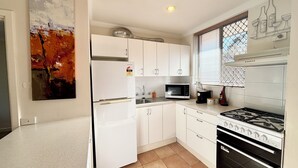 A compact kitchen with white cabinets, a microwave, a gas stove, and a window with blinds. - City Escape Getaway Subiaco 1Bedrm Unit (Subiaco)