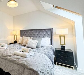 Een slaapkamer met een groot bed, twee nachtkastjes met lampen, een hoofdbord en een raam.