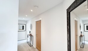 A hallway with a wooden door, a framed picture on the wall, and a small table with a vase.