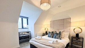 Een slaapkamer met een groot bed, twee nachtkastjes, een kroonluchter en een raam.