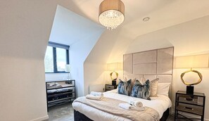 A bedroom with a large bed, two bedside tables, a chandelier, and a window.