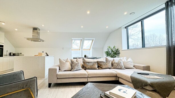 Een moderne woonkamer met een hoekbank, een salontafel en een keuken op de achtergrond.