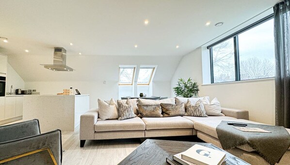 A modern living room with a sectional sofa, a coffee table, and a kitchen in the background.