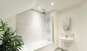 A modern bathroom with a glass-enclosed shower, a white sink, and a potted plant.