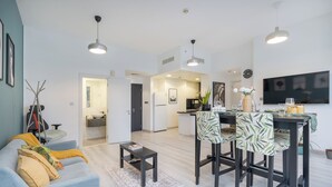 A modern apartment with a living room, dining area, and kitchen. There is a sofa with cushions, a coffee table, and a dining table with chairs. The kitchen has a refrigerator, stove, and microwave. - New Listing | JBR Beach Gem | Czechin | 1BD (Dubai)