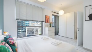 A modern hotel room with a large bed, a view of the city, a wardrobe, and a vanity with a mirror. - New Listing | JBR Beach Gem | Czechin | 1BD (Dubai)
