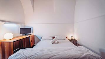 Ein Hotelzimmer mit einem Bett, einem Schreibtisch mit Computer, einer Lampe und einem Nachttisch ebenfalls mit Lampe.