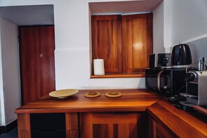 Une cuisine compacte dotée d’un plan de travail en bois, d’un four à micro-ondes, d’une machine à café et d’une fenêtre avec des stores en bois.
