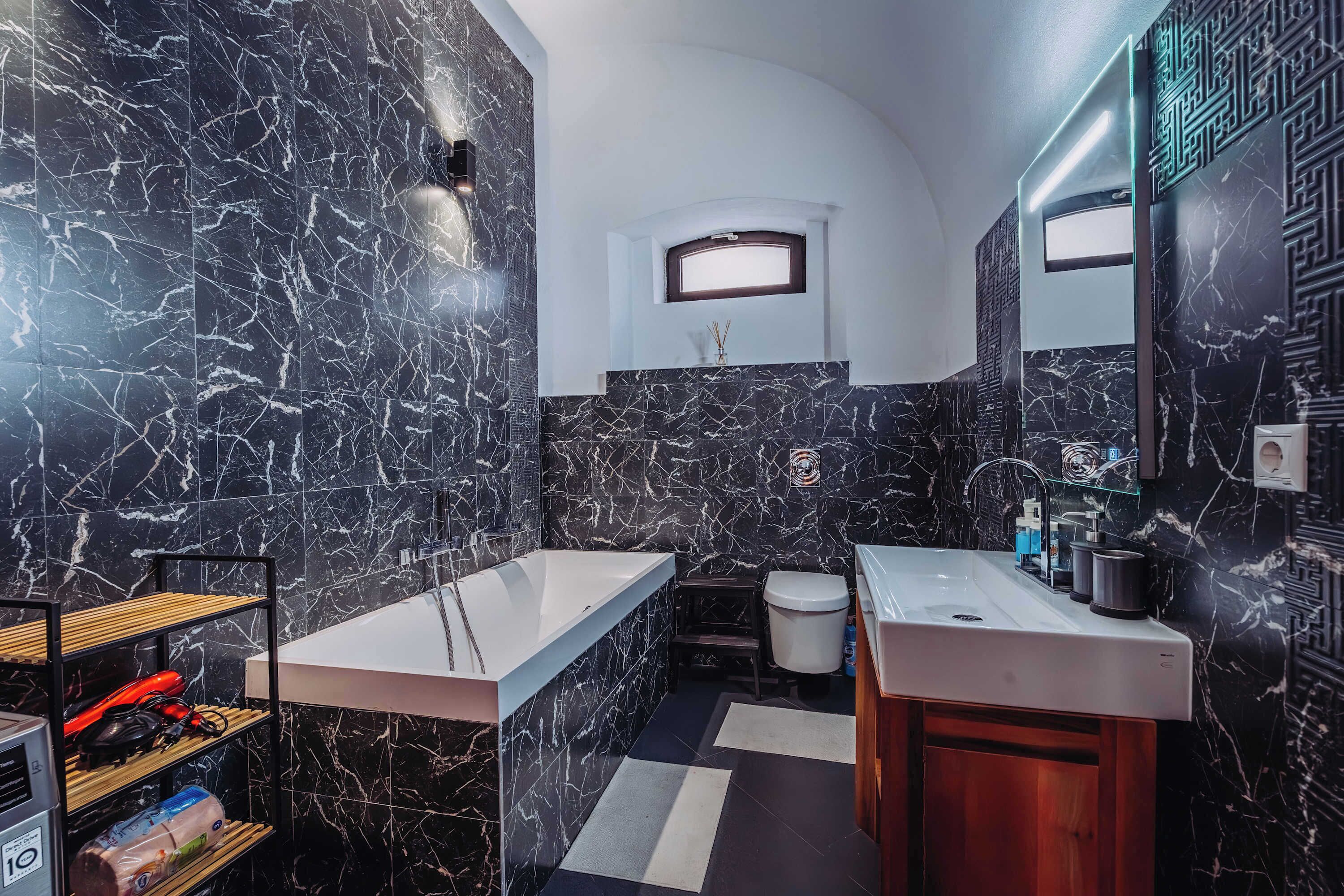 A modern bathroom with a marble backsplash, a freestanding bathtub, a vanity with a sink, and a toilet.