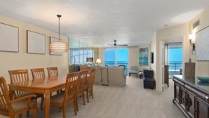 A spacious living area with a wooden dining table and chairs, a sofa, and a view of the ocean. - Beachfront 2BR, 2BA condo with heated pool and beach access. (Marco Island)