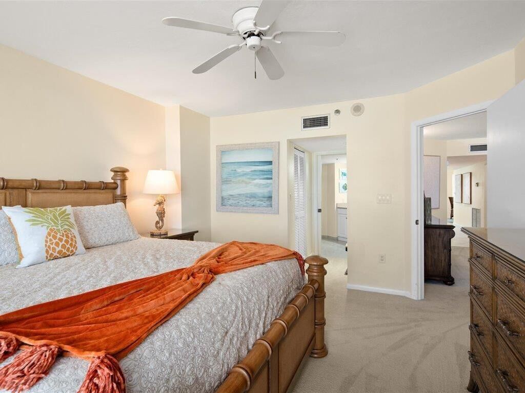 A bedroom with a bed, a ceiling fan, a nightstand, a lamp, a dresser, and a door leading to another room.