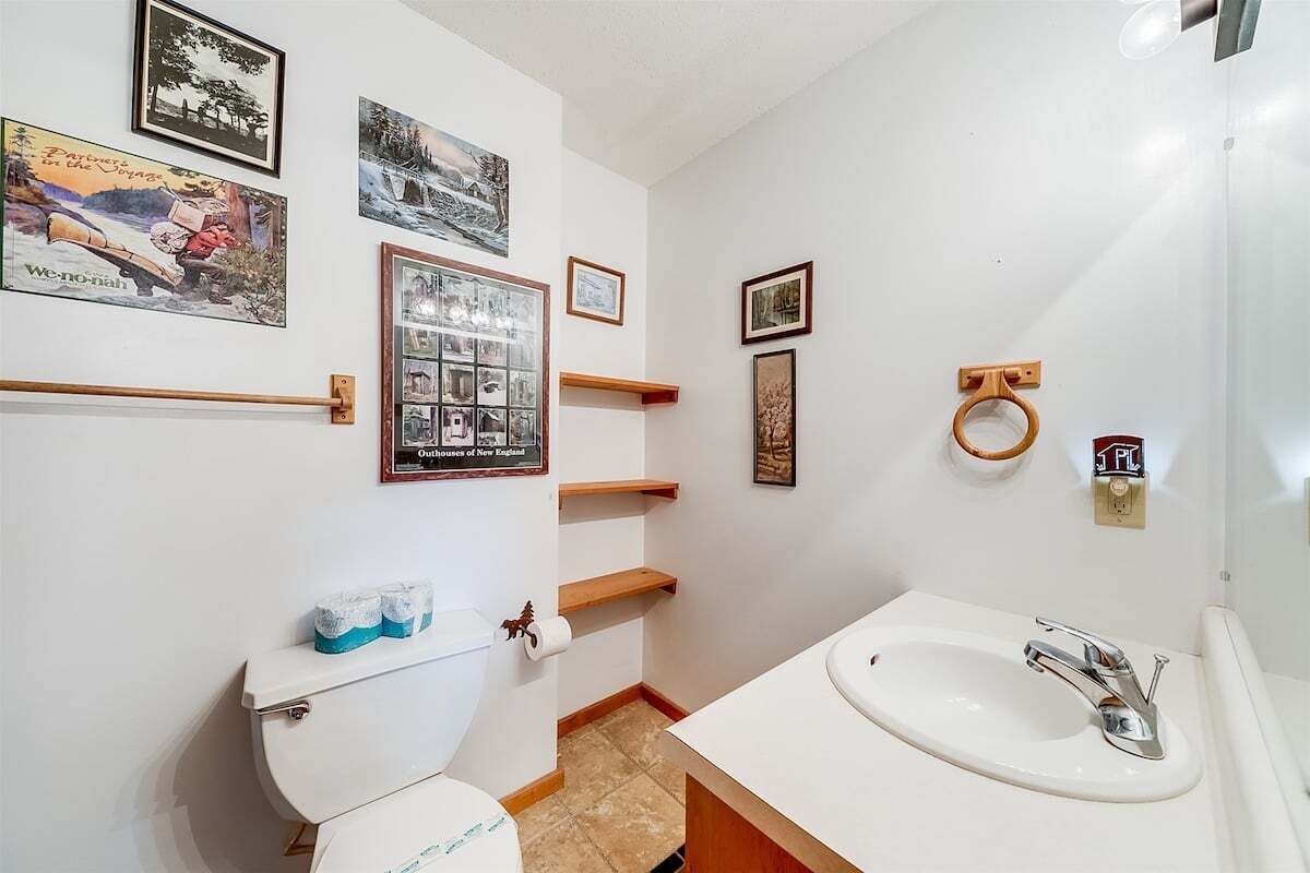 A bathroom with a toilet, sink, and framed pictures on the wall.
