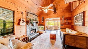 Interno di una baita di legno con camino, pareti in legno, ventilatore a soffitto e testa di cervo appesa al muro.