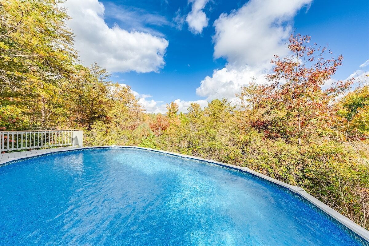 A clear blue swimming pool surrounded by trees with autumn foliage.