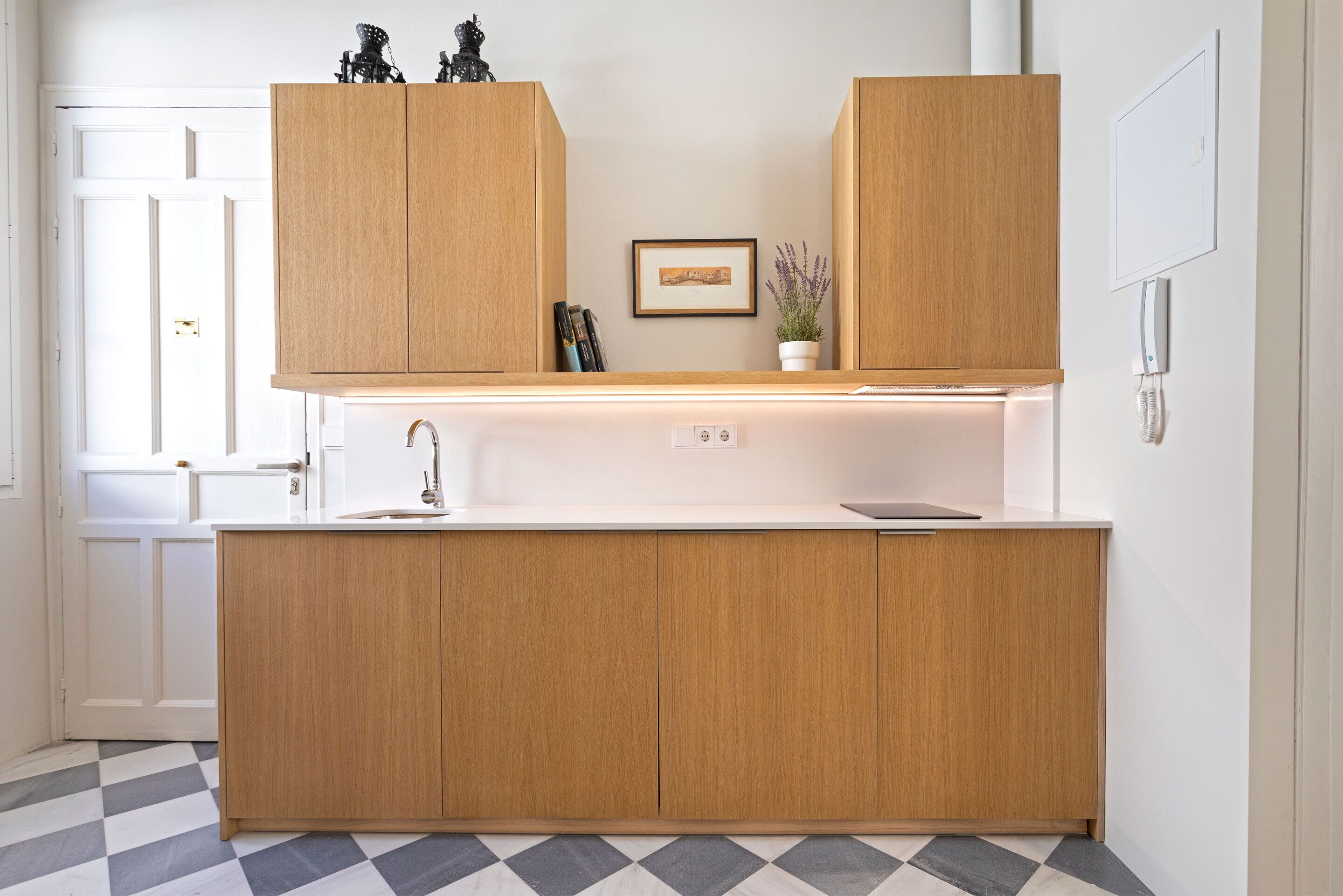 A modern kitchen with wooden cabinets, a white countertop, and a checkered floor.