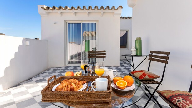 Ein Frühstücksbuffet auf einem Balkon mit Croissants, Orangensaft und einem Korbwäschesystem.