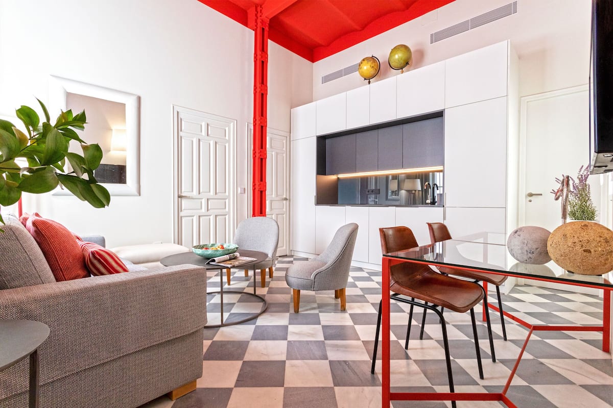 Una sala moderna con piso a cuadros, un sofá, una mesa de centro y un comedor con sillas y una mesa de vidrio.