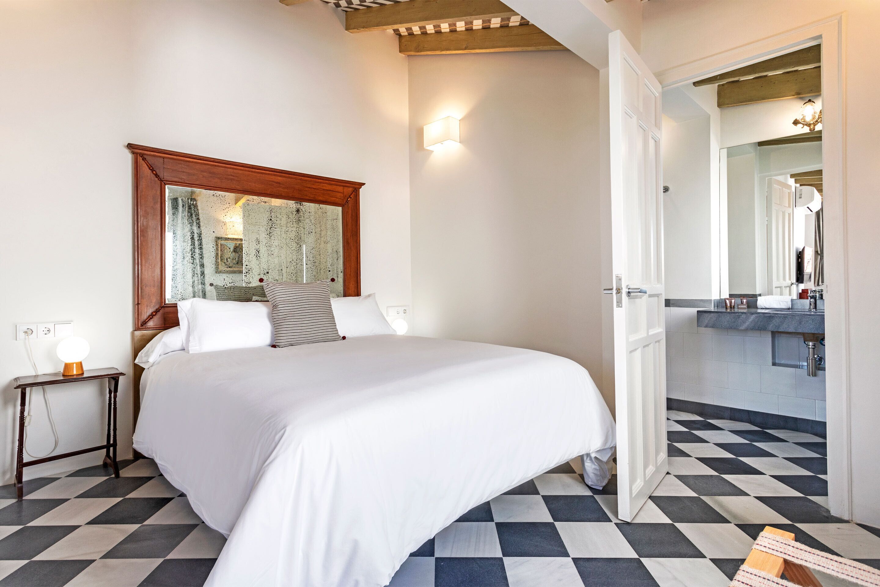 A hotel room with a bed, bedside table, and a bathroom visible through an open door.
