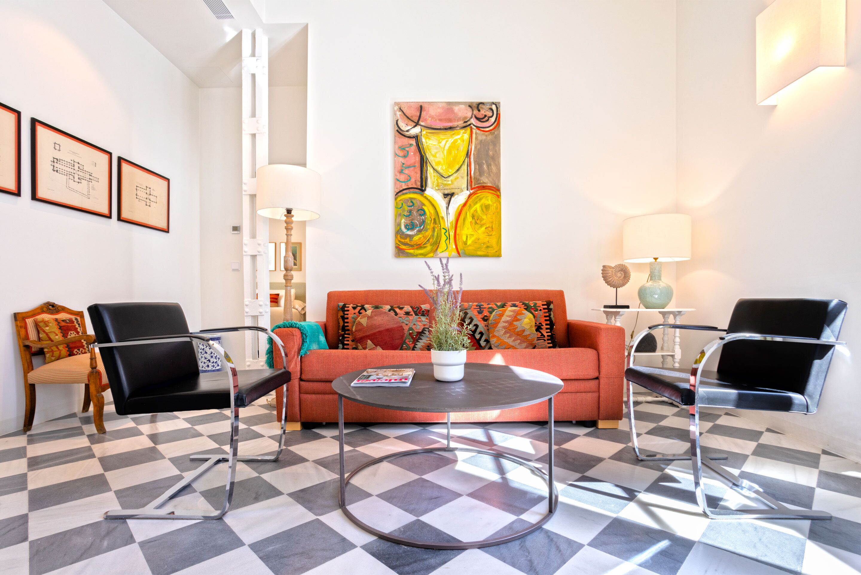 Una sala de estar moderna con piso a cuadros, un sofá, dos sillones, una mesa de centro redonda y un cuadro en la pared.