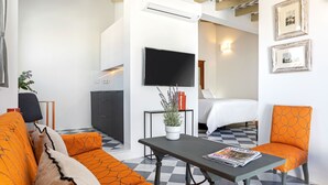 Ein modernes Hotelzimmer mit Schachbrettboden, einer Couch, einem Tisch mit einer Zeitschrift, einem Bett, einem Fernseher und einer Topfpflanze.