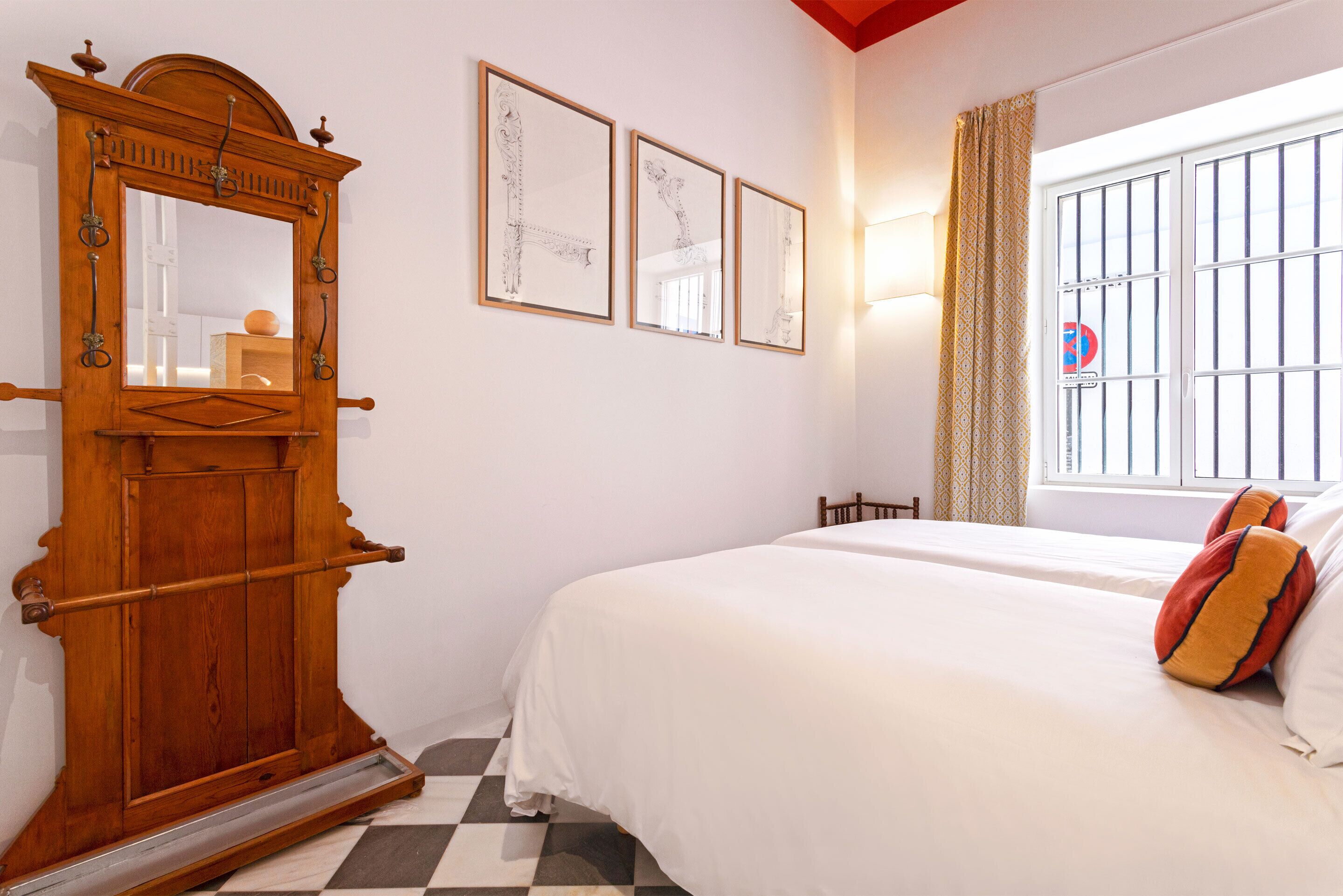 A bedroom with a large wooden wardrobe, a bed with white bedding and two pillows, and three framed artworks on the wall.