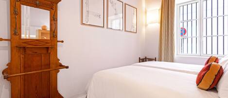 A bedroom with a large wooden wardrobe, a bed with white bedding and two pillows, and three framed artworks on the wall.