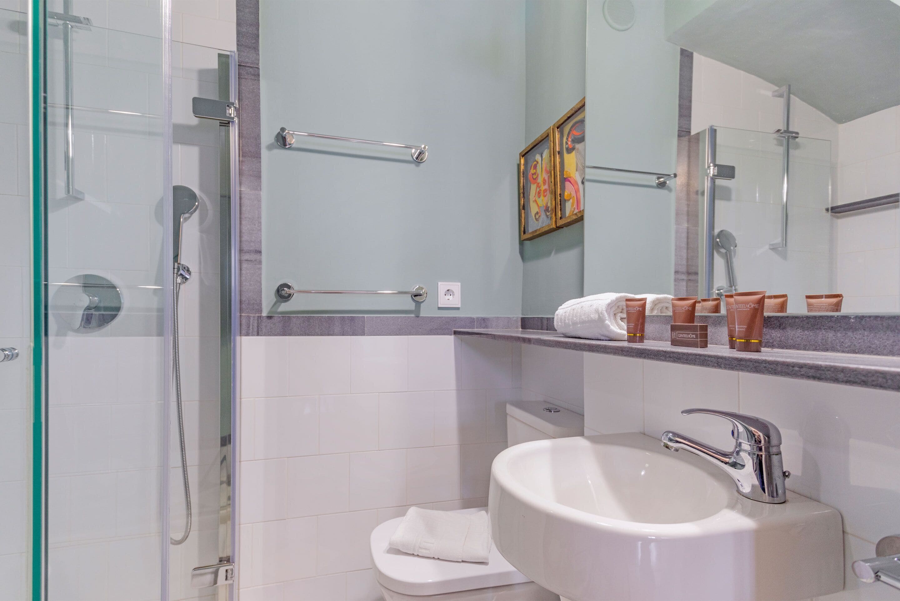 Un baño moderno con ducha acristalada, lavamanos blanco con grifo cromado y encimera de mármol.