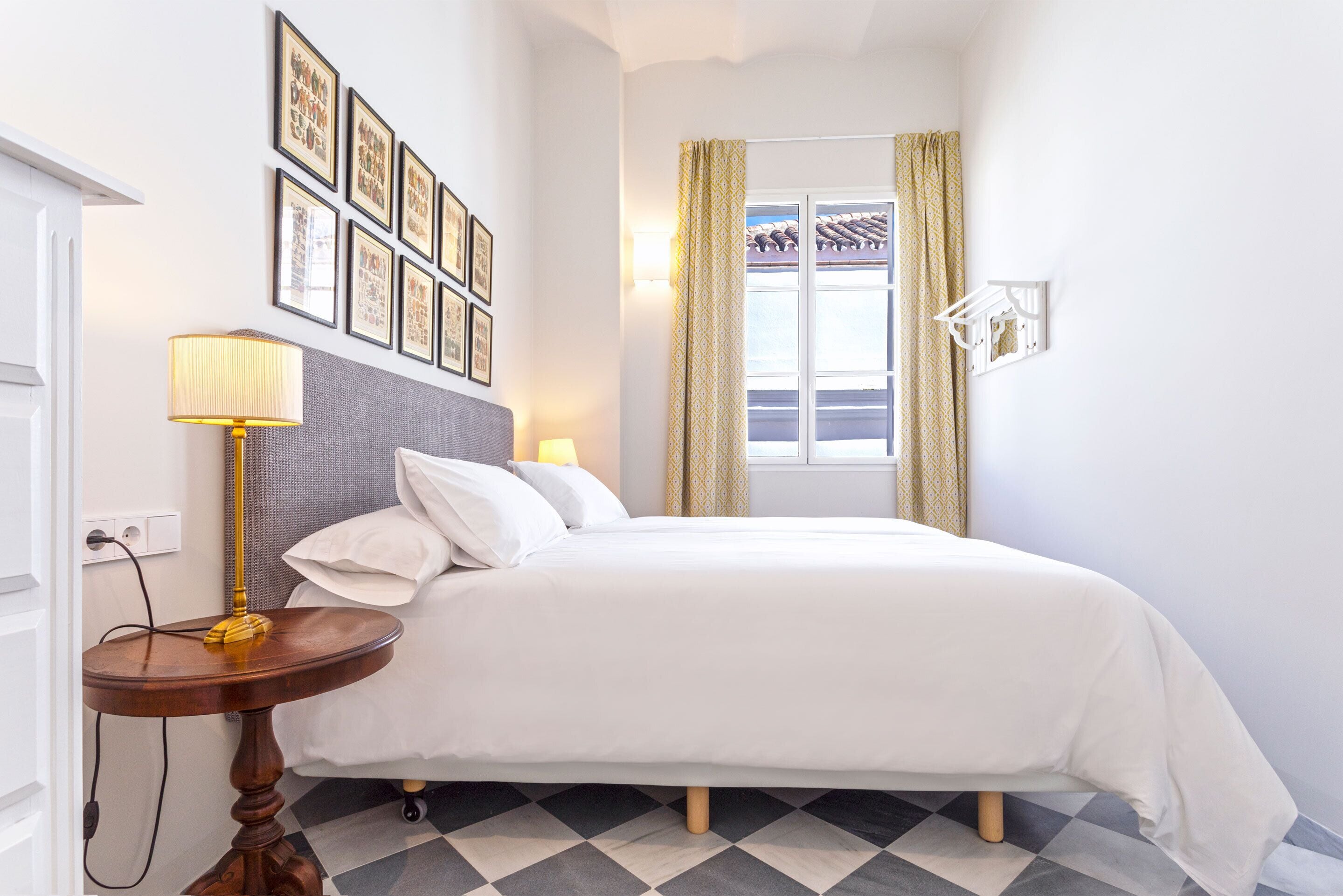 Un dormitorio ordenado con cama, mesita de noche, lámpara y cuadros en la pared.