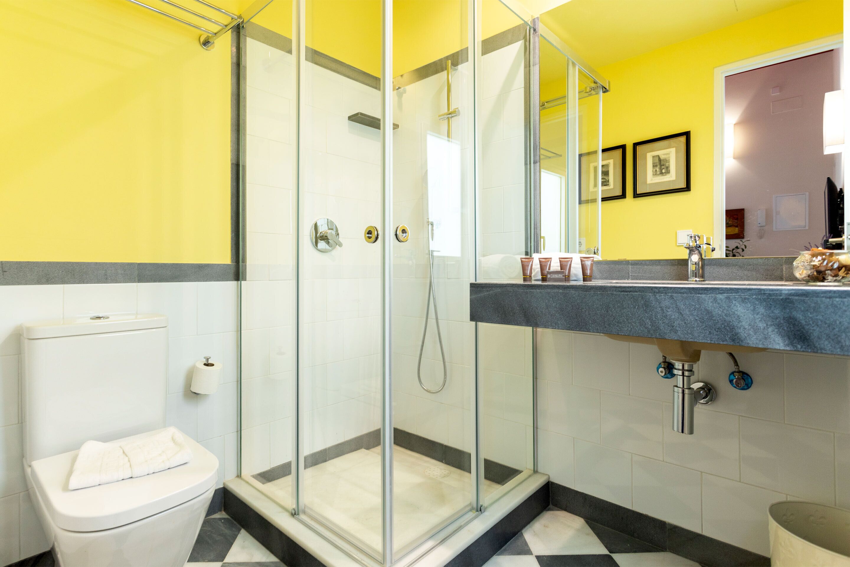 A bathroom with a glass-enclosed shower, a toilet, and a sink with a mirror above it.
