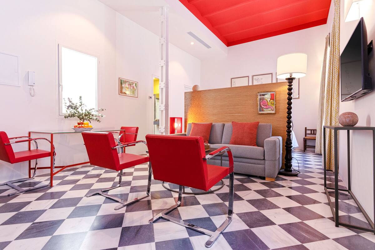 Una sala de estar moderna con suelo de cuadros, sillas rojas, un sofá gris y un cabecero de madera.