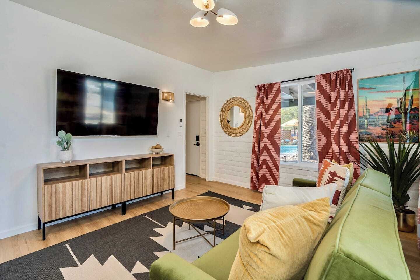 Uma sala de estar moderna com televisão de tela plana, rack de madeira, sofá verde e mesa de centro redonda.