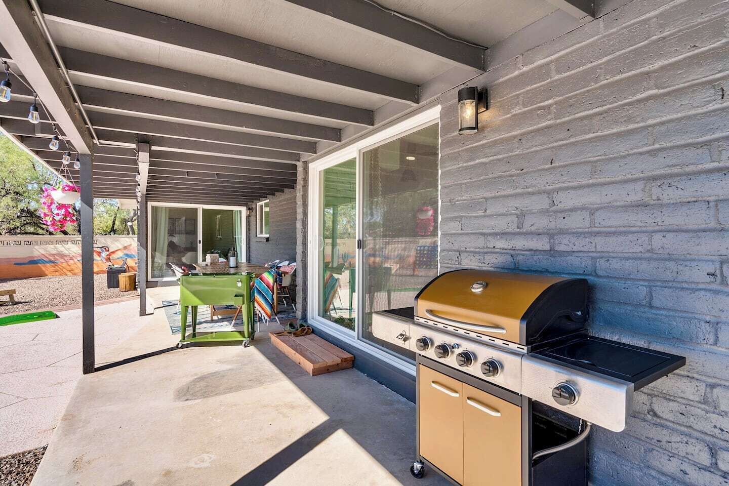 Een terras buiten met een ingebouwde barbecue, een overdekte zithoek en een glazen deur naar een afgedekte ruimte.