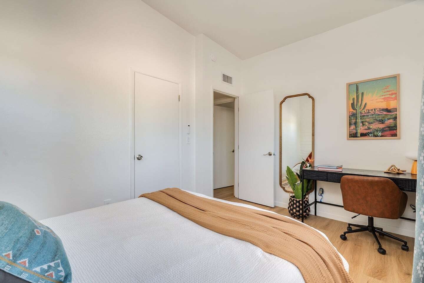 A bedroom with a bed, a desk, a chair, and a large mirror.