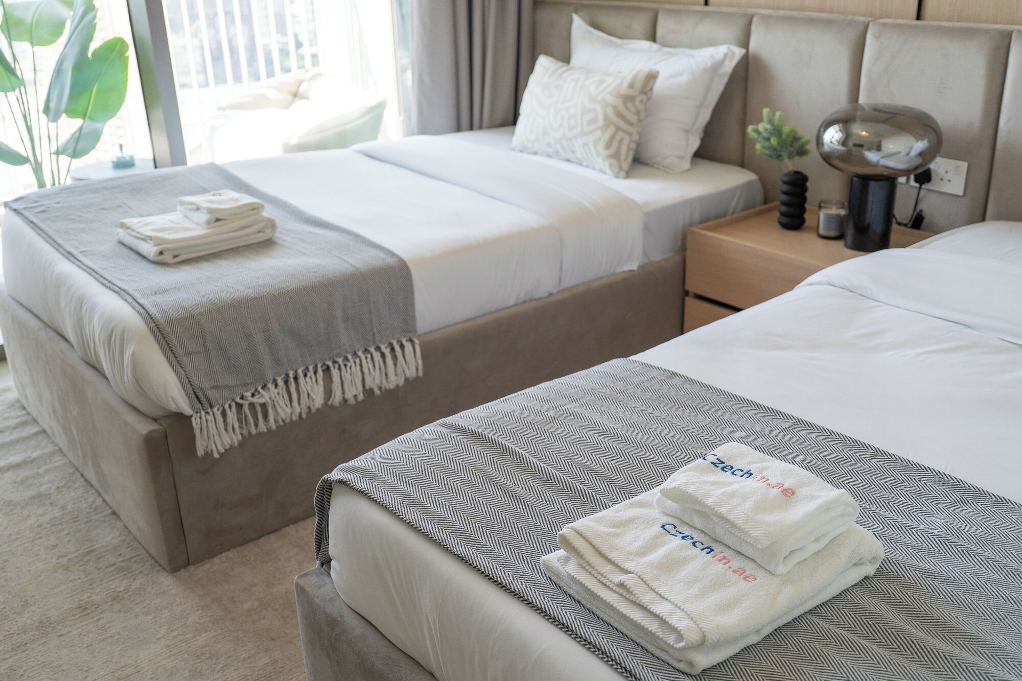 A hotel room with two beds, a nightstand, and a lamp.