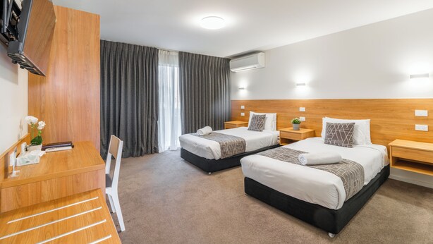 A hotel room with two beds, a desk, a chair, a TV, and a window with curtains. - Rainbow Motel Queanbeyan (Queanbeyan East)