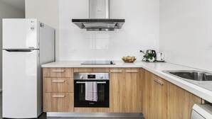 A modern kitchen with white cabinetry, a stainless steel range hood, a built-in oven, and a sink. - Rainbow Motel Queanbeyan (Queanbeyan East)