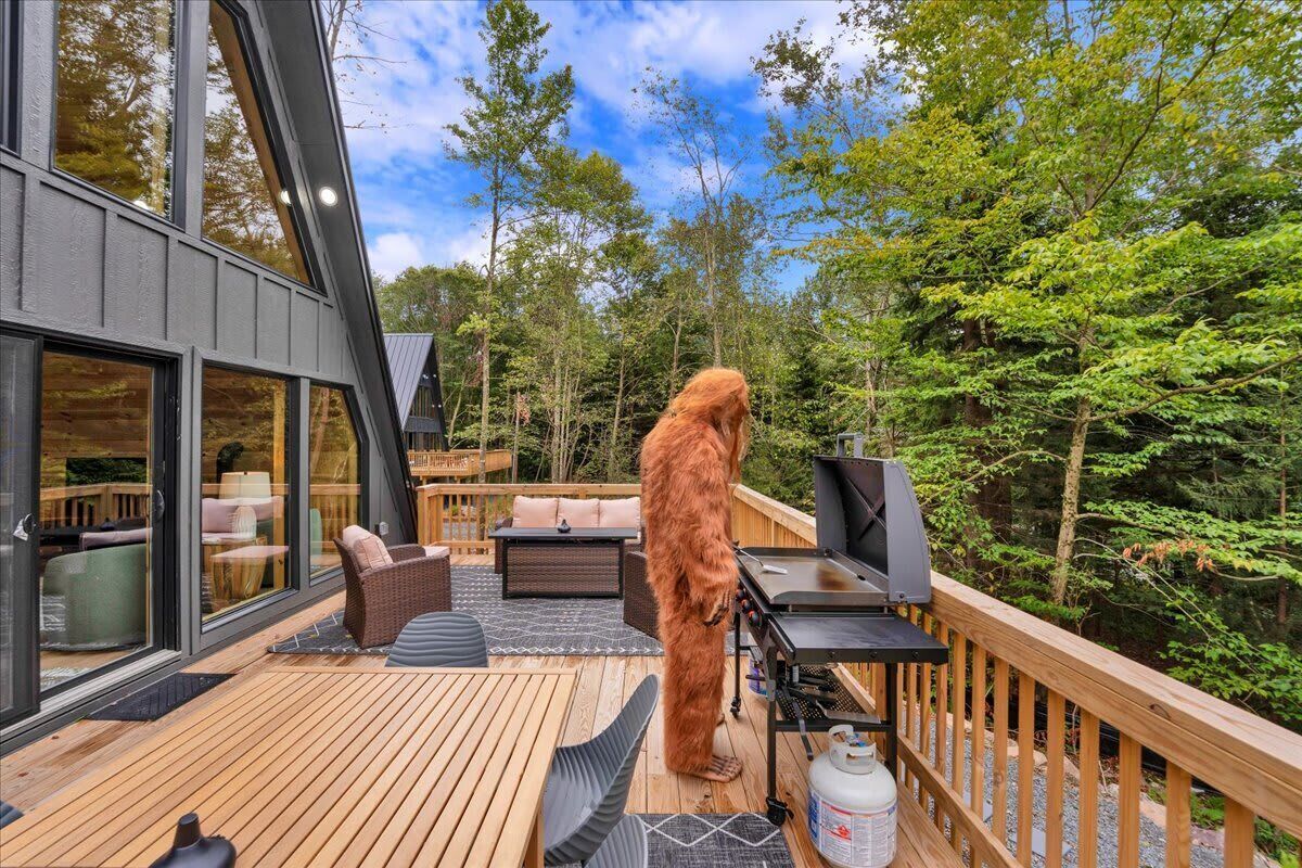 Una terraza con mobiliario exterior, una parrilla y un ventanal grande con vista a un área boscosa.