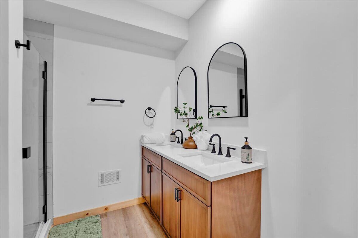 A modern bathroom with a white sink, wooden vanity, black fixtures, and a mirror.