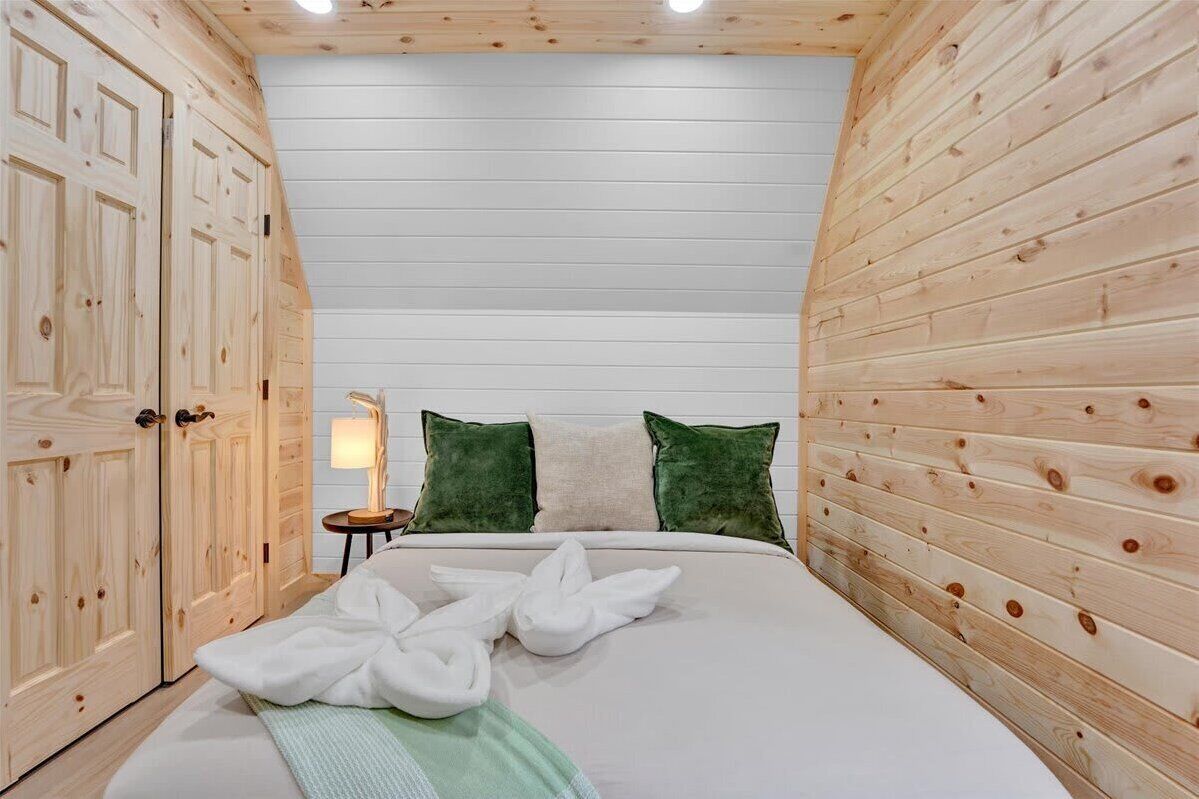 A wooden-paneled room with a bed, two green pillows, and a bedside lamp.