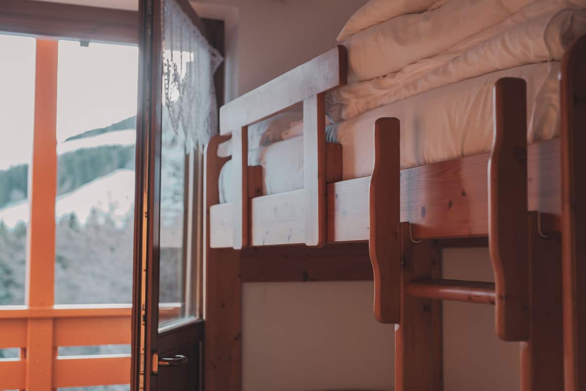 A bunk bed with a wooden frame and a window with a view of a snowy landscape.